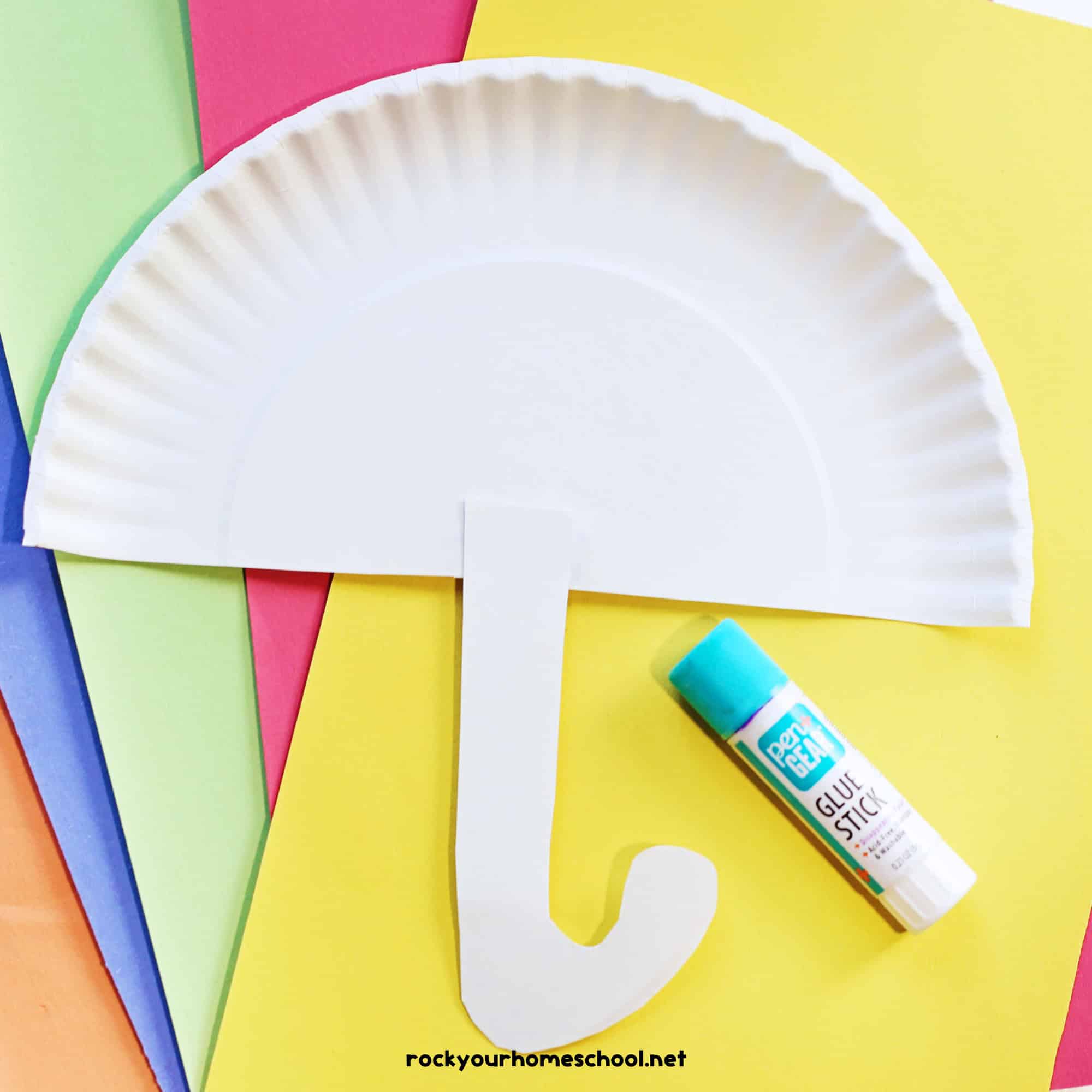 Half paper plate with J-shaped handle and glue stick on construction paper.