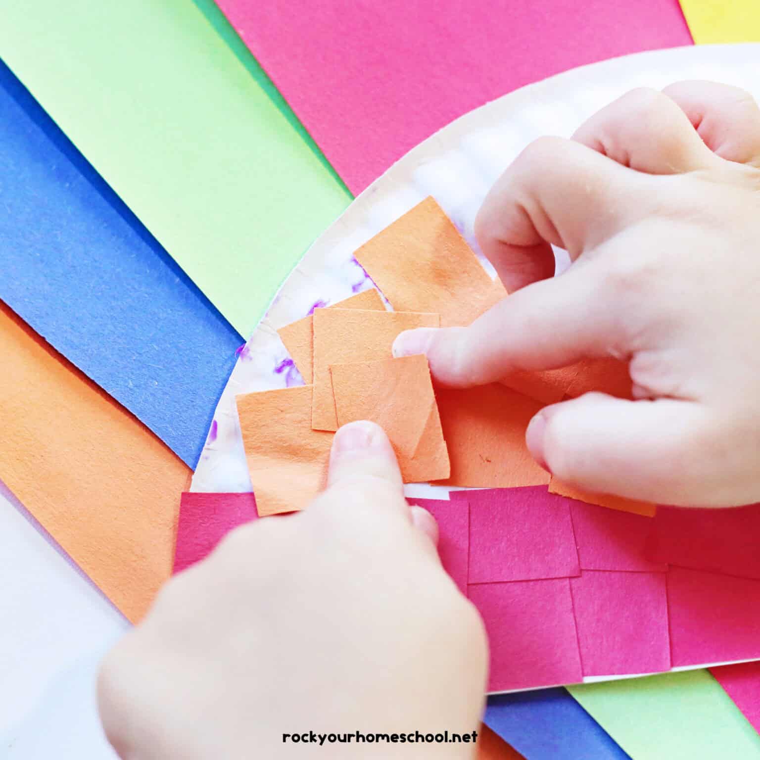 Child adding orange paper squares to paper plate craft.