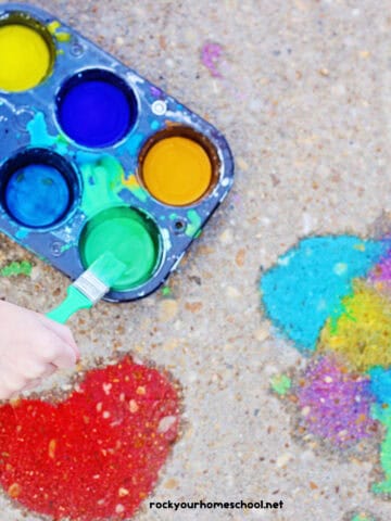 Child using green paint brush with muffin tin tray of DIY sidewalk chalk paints.