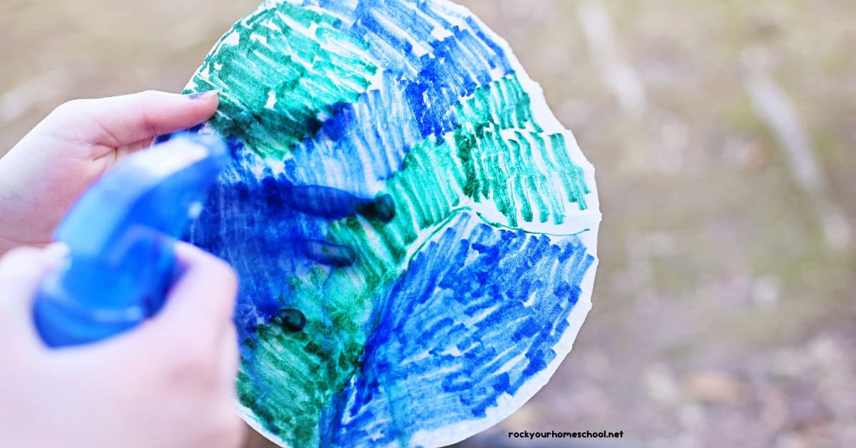 Person using blue spray bottle with water on coffee filter colored green and blue.