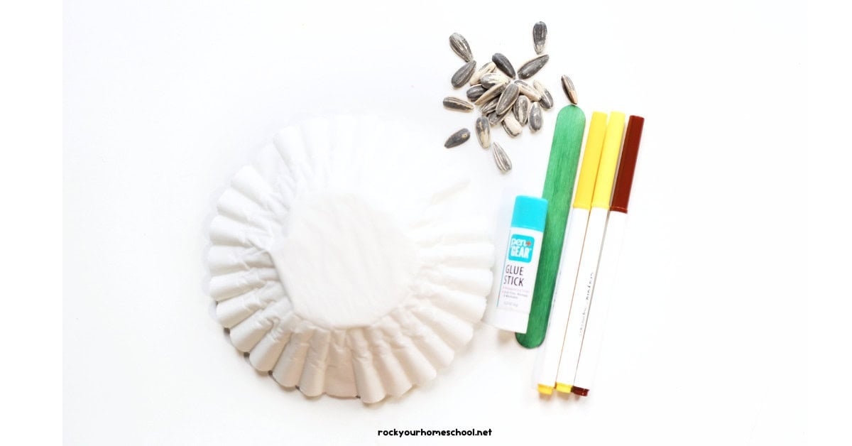 Coffee filters, sunflower seeds, glue stick, green wood craft stick, and yellow and brown markers.