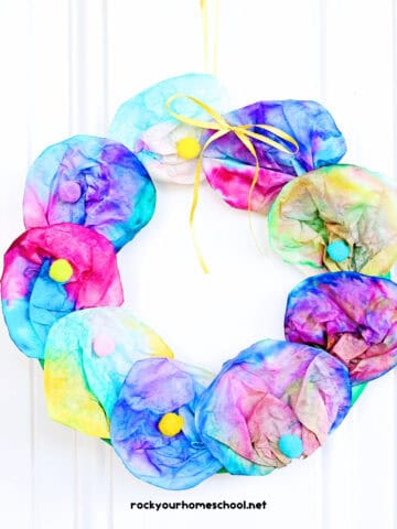 Example of colorful coffee filter wreath craft for kids made with paper plate, pom poms, and ribbon.