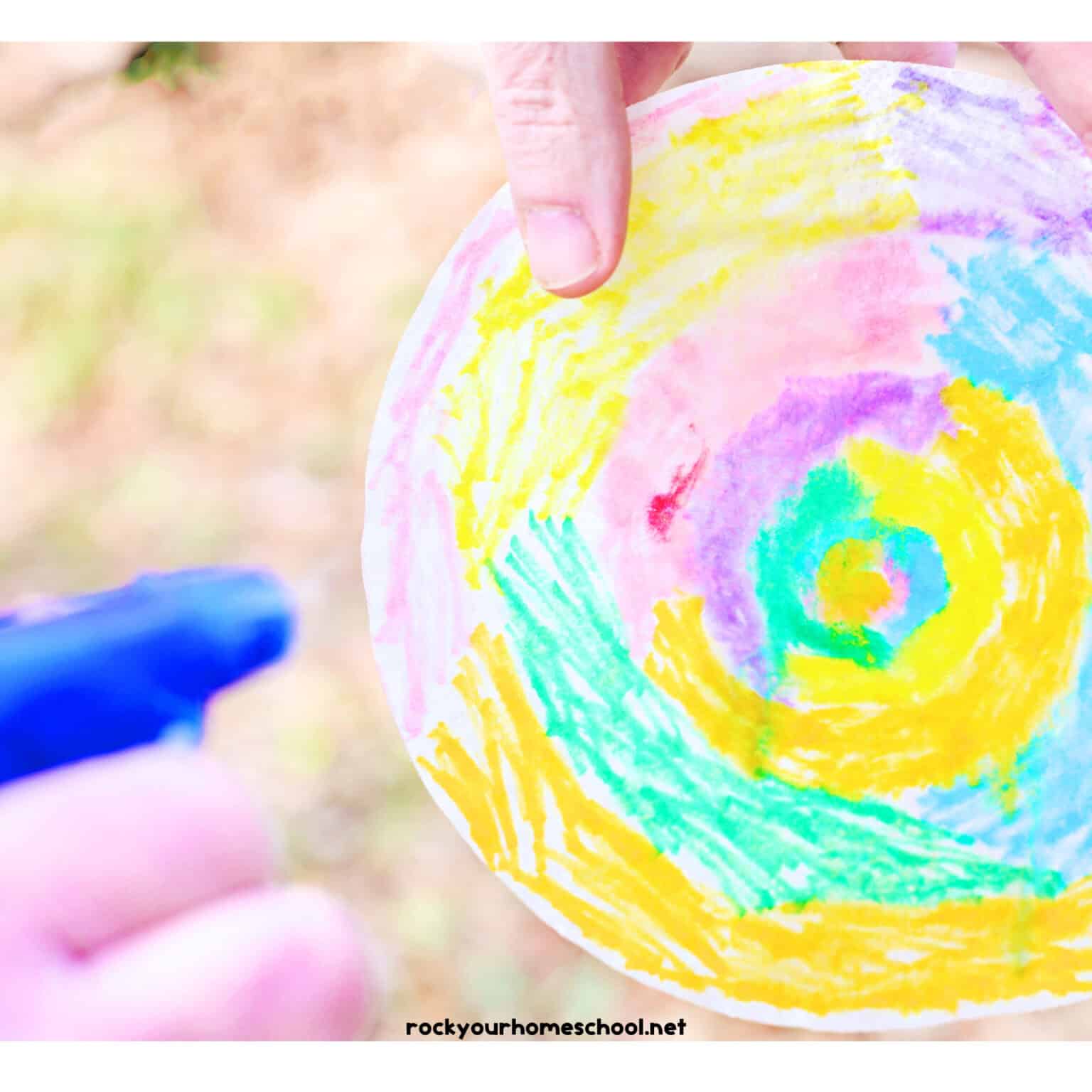 Person using blue spray bottle to spray water on coffee filter colored with markers.