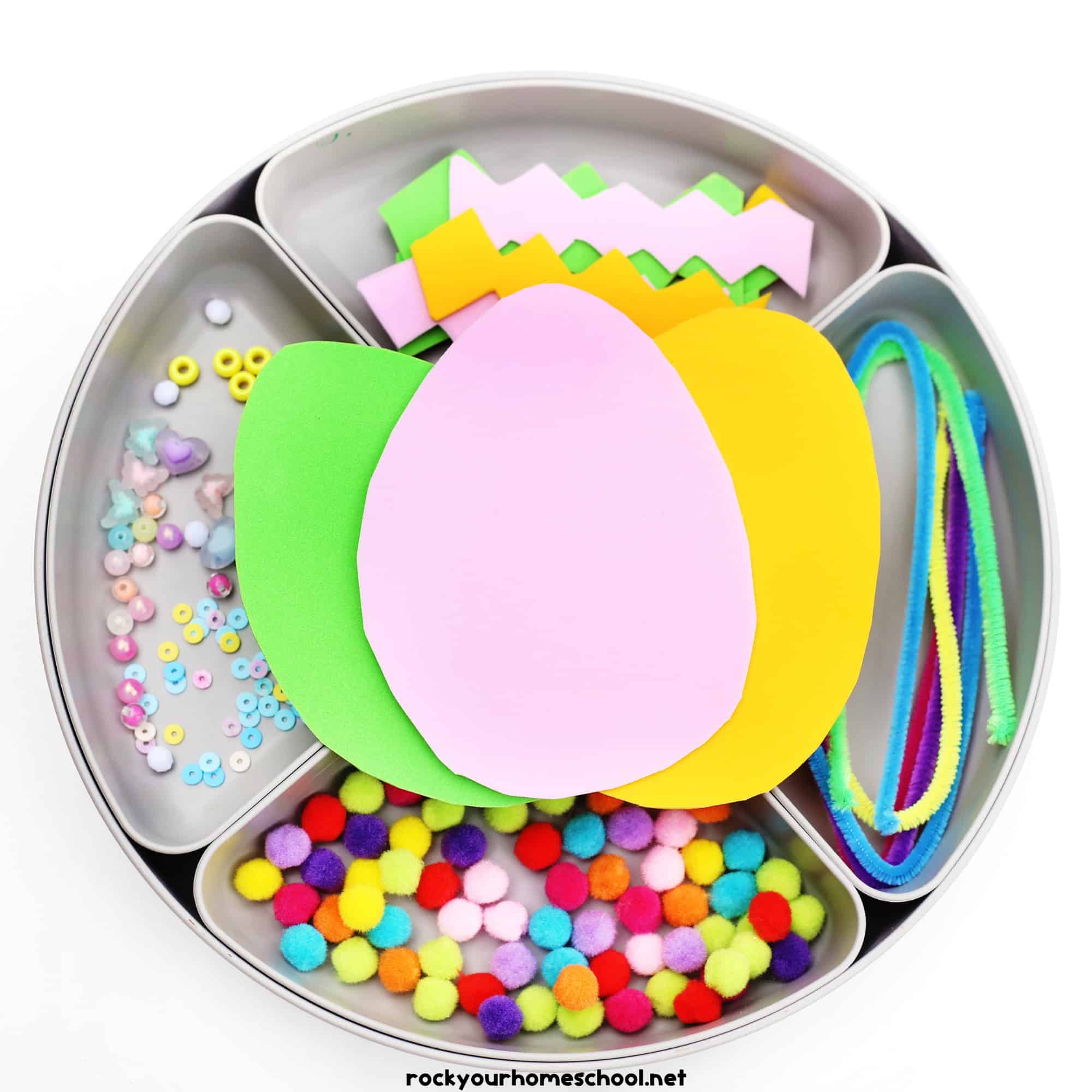 Activity tray with egg foam sheets, pipe cleaners, pom poms, beads, and other decorations.