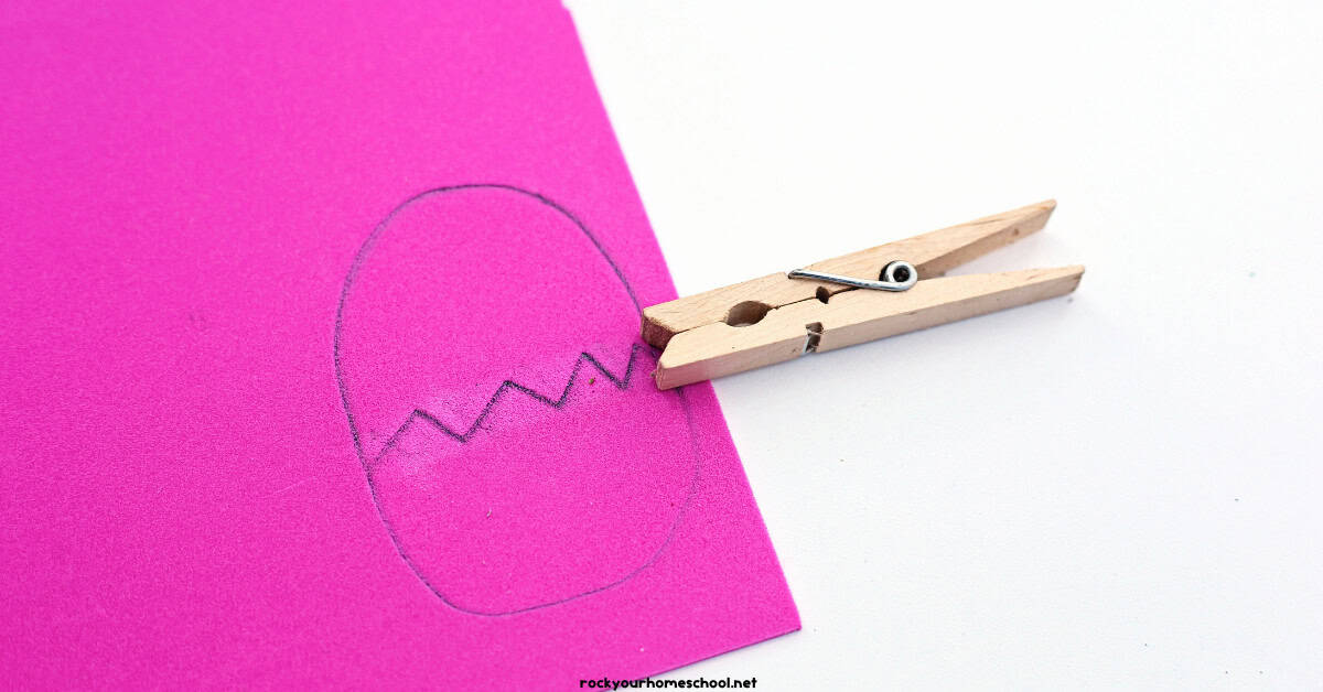 Pink foam sheet with egg cracked in half drawn with pencil and clothespin.