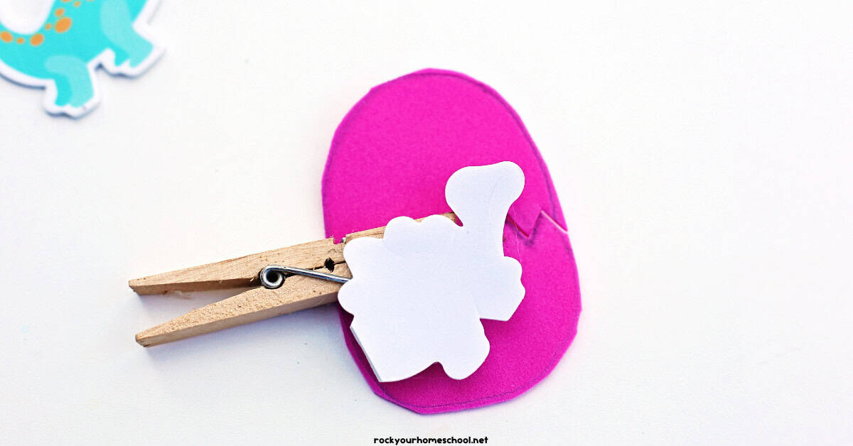 Back of dinosaur sticker on pink foam egg with clothespin.