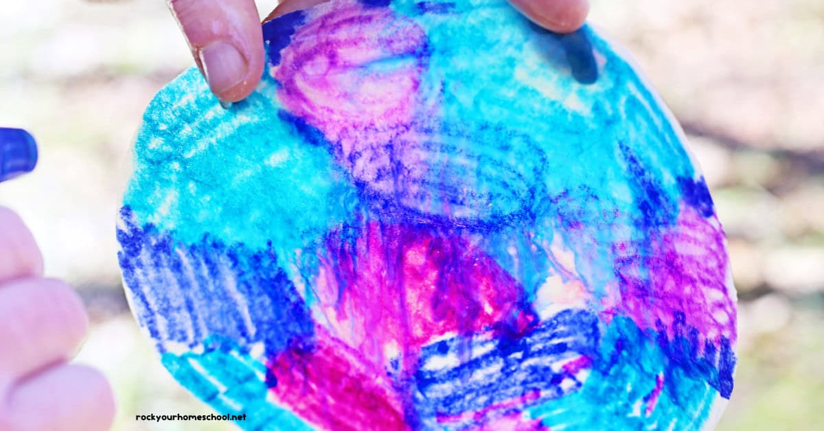 Person using blue spray bottle to spray water on coffee filter colored with markers.