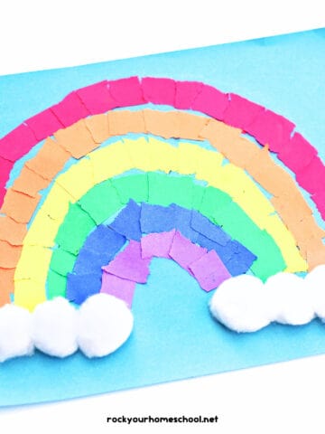 Example of torn paper rainbow craft with cotton balls on light blue paper.