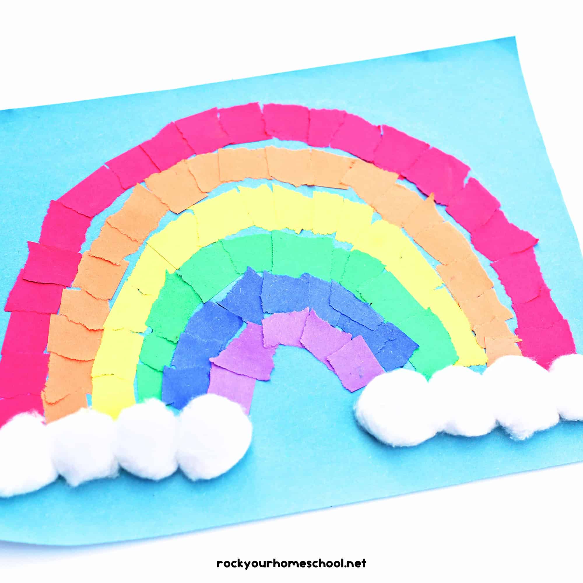 Example of torn paper rainbow craft with cotton balls on light blue paper.