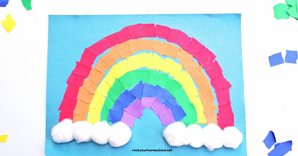 Example of torn paper rainbow craft on light blue construction paper with cotton ball clouds.