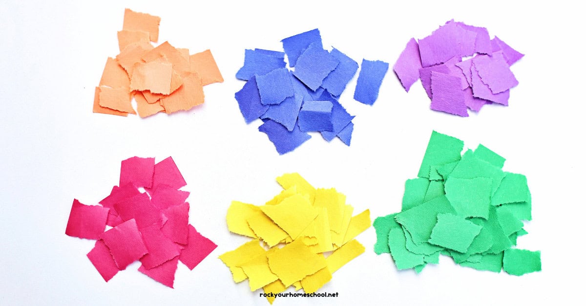 Piles of construction paper torn into pieces in orange, blue, purple, red, yellow, and green.