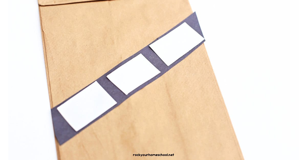 Brown paper bag with black and white construction paper bandolier.