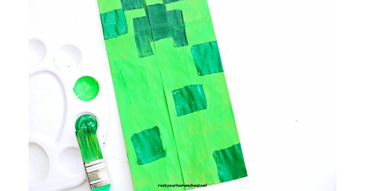 Bottom of green Creeper paper bag craft with green paint brush and paint.