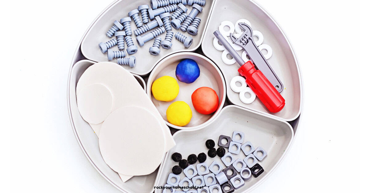 Activity tray with white foam sheets, black pom poms, yellow, blue, and red playdough balls, and plastic nuts and bolts, screwdriver, and wrench.