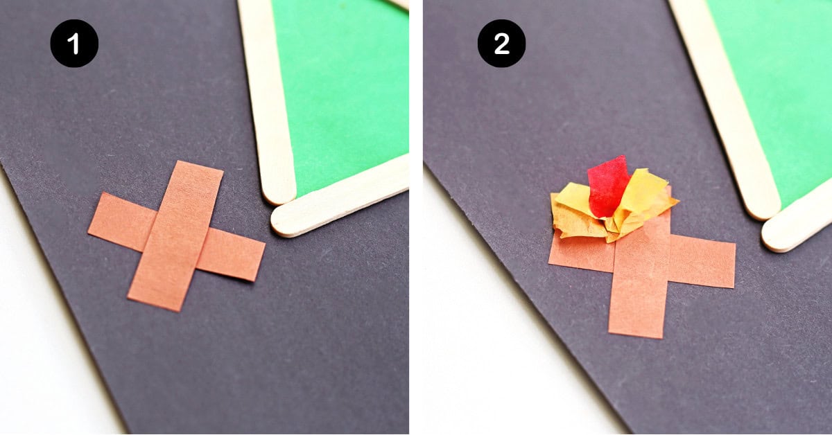Brown construction paper in shape of X with red, orange, and yellow tissue paper on black construction paper. 
