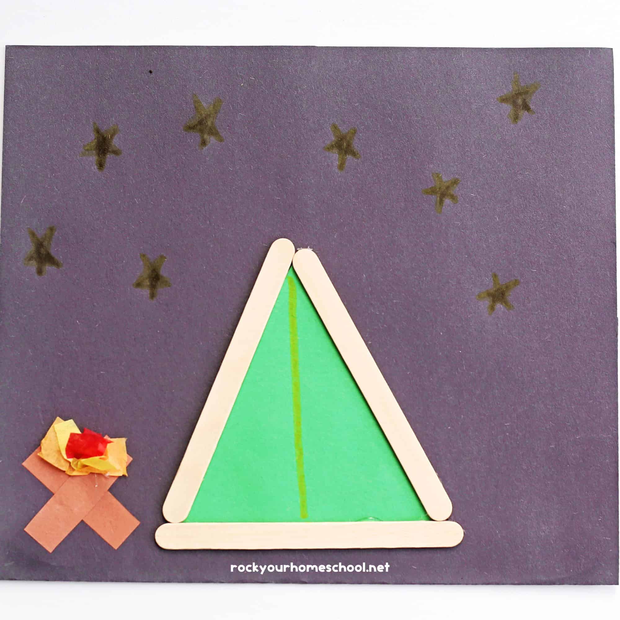 Example of simple popsicle stick tent craft on black construction paper with paper campfire.