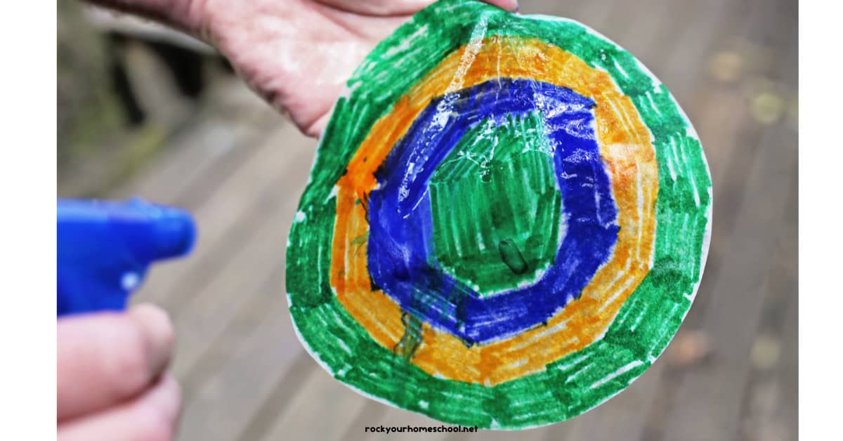 Coffee filter colored green, yellow, and blue being sprayed with water.