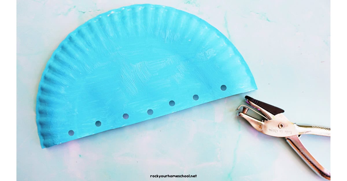 Half paper plate painted light blue with hole punch.