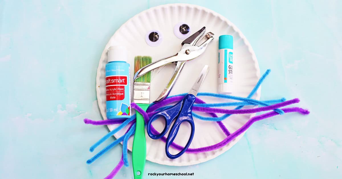 Paper plates, googly eyes, hole punch, glue stick, blue paint, paint brush, scissors, and blue and purple pipe cleaners.