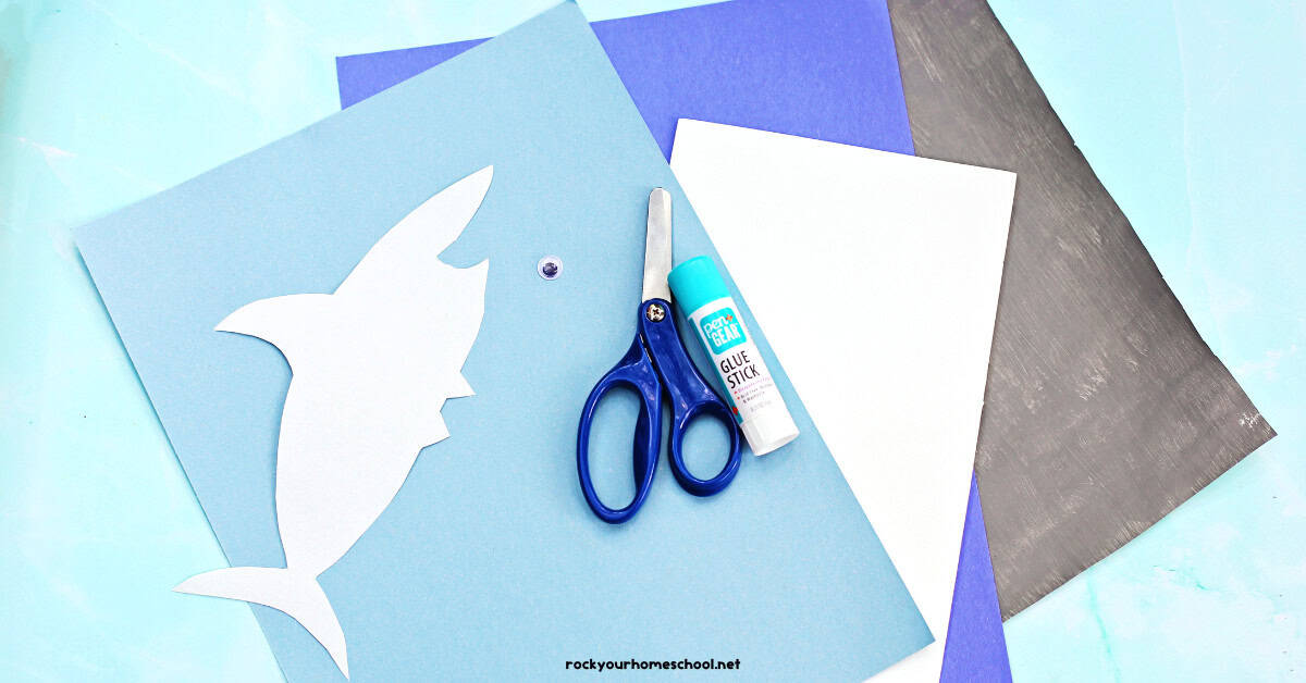 Light blue, blue, and white construction paper, scissors, and glue stick with paper painted gray.