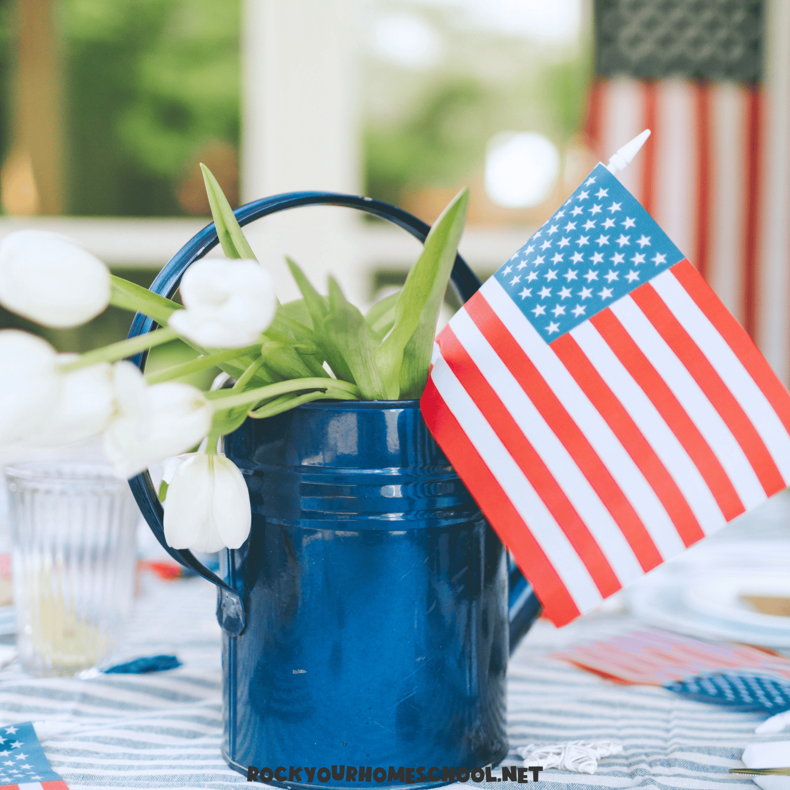 American flag in blue pitcher with white flowers on table decorated for 4th of July to feature July homeschool ideas.