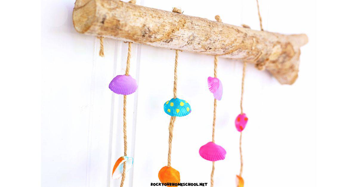 Close-up of DIY seashell wind chimes craft for kids made with drift wood, twine, and painted shells.