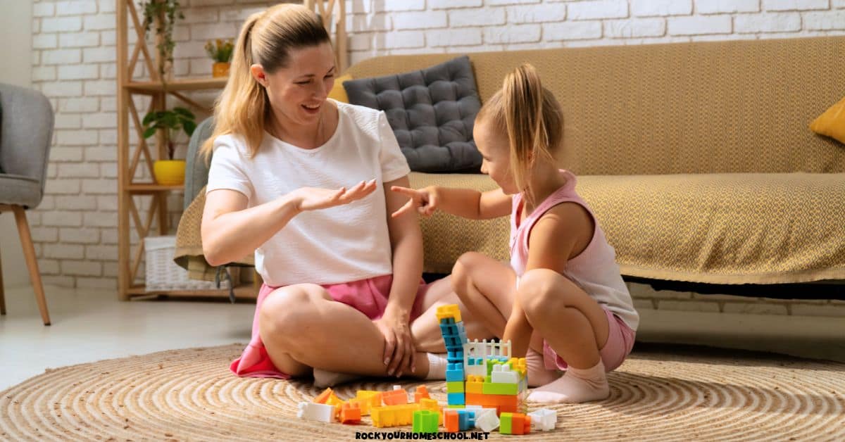 Mother and daughter sitting on rug with blocks and playing hand game.