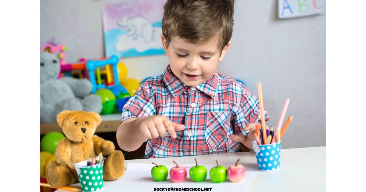 Preschool boy smiling as he counts toy apples.