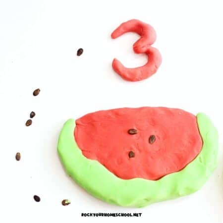 Homemade watermelon playdough in red and light green with watermelon seeds.