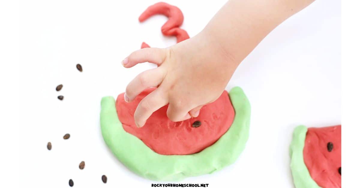 Child pressing watermelon seeds into homemade red watermelon playdough.