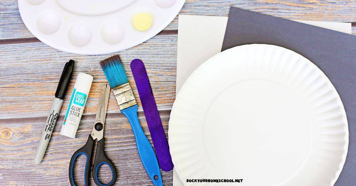 Paper plate, black and white paper, purple wood craft stick, paint brush, scissors, glue stick, black marker, and yellow paint.
