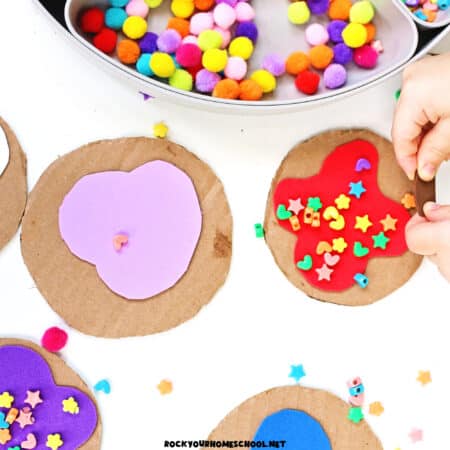 Child working on cookie decorating activity tray with cardboard circles, foam shapes, pom poms, and more.