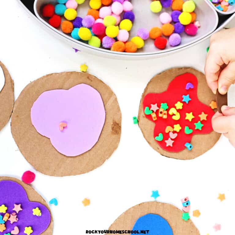 Child working on cookie decorating activity tray with cardboard circles, foam shapes, pom poms, and more.