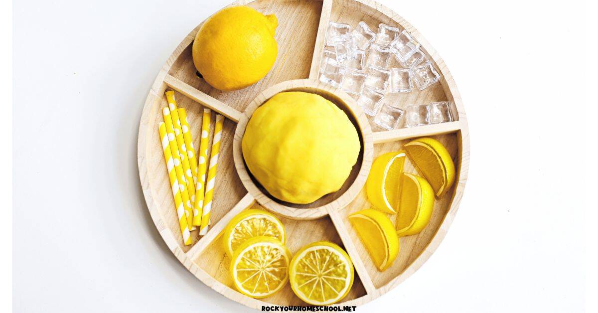 Easy lemon playdough on activity tray with lemon, plastic lemon slices, paper straws, and play ice.