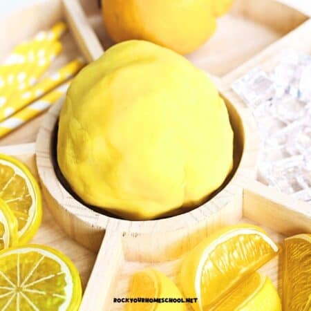 Easy homemade lemon playdough on activity tray with plastic lemons and paper straws.
