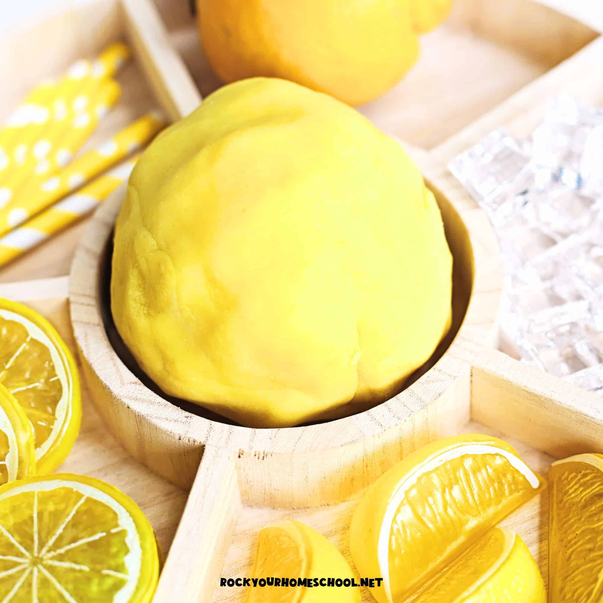 Easy homemade lemon playdough on activity tray with plastic lemons and paper straws.