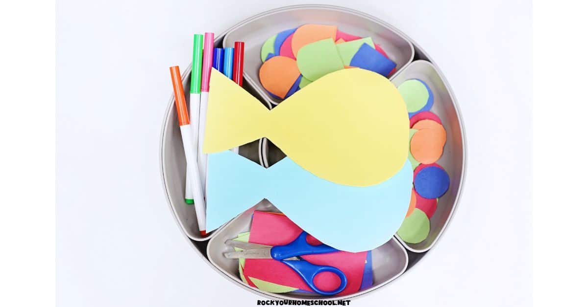 Two paper fish on activity tray with markers, scissors, and colorful pieces of paper.