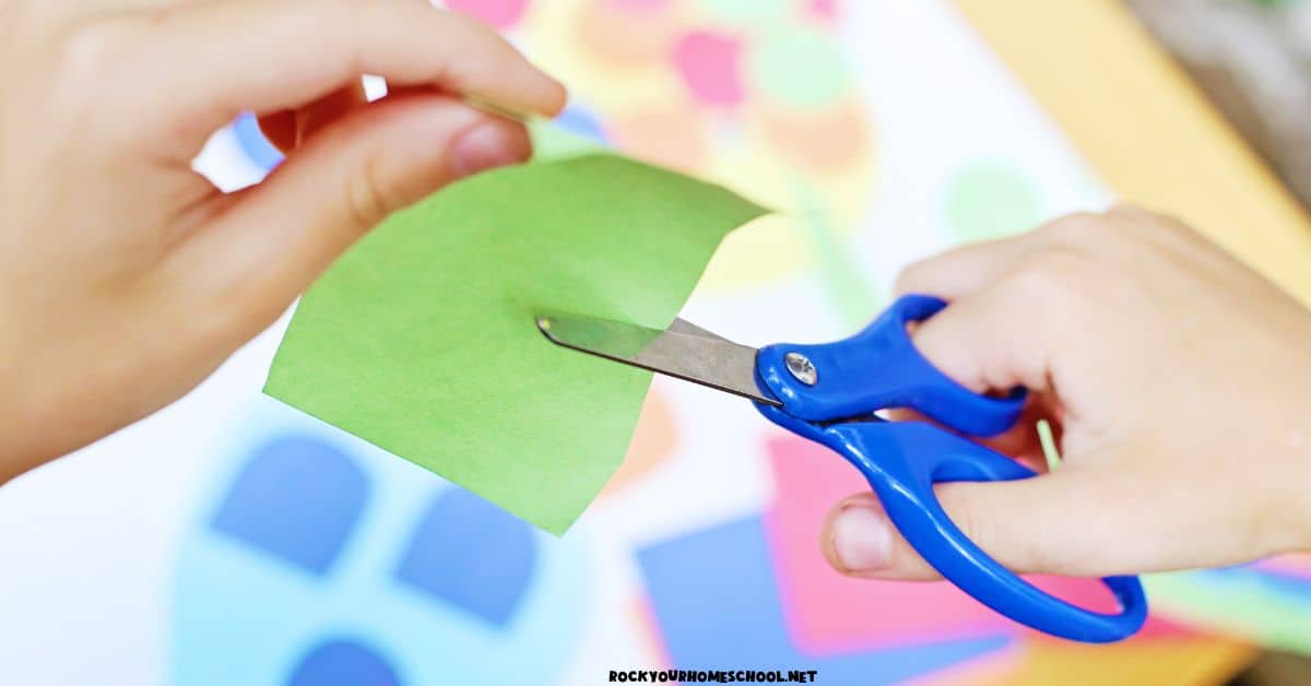 Child using scissors to cute green construction paper.