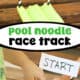 Green pool noodle, craft knife, scissors, paper straw, tape, and white paper and boys using toy car and marbles on DIY pool noodle race track.