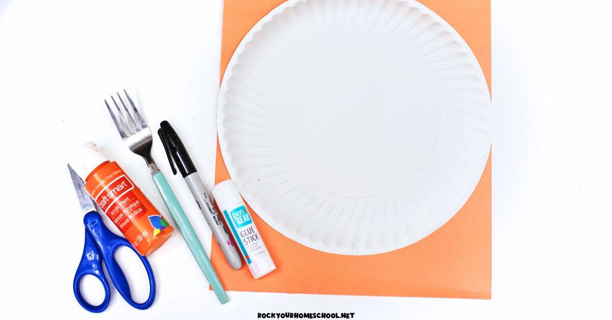 Orange construction paper, white paper plate, scissors, orange paint, fork, black marker, and glue stick.