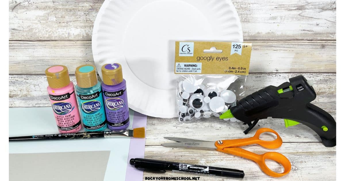 Paper plate, googly eyes bag, glue gun, scissors, black marker, cardstock in gray, light blue, and light purple, paint brush, and paint bottles in pink, aqua, and purple.