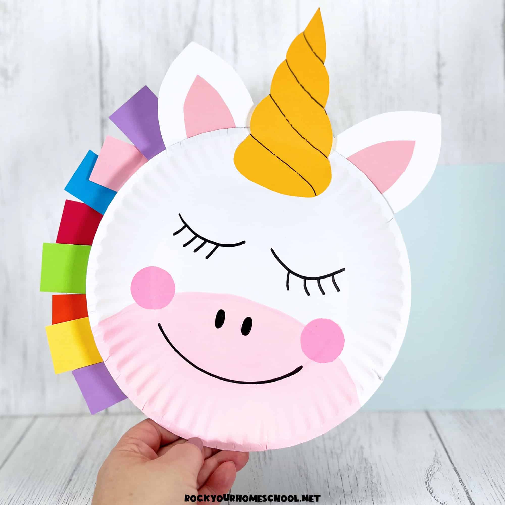 Woman holding example of paper plate unicorn craft for kids.