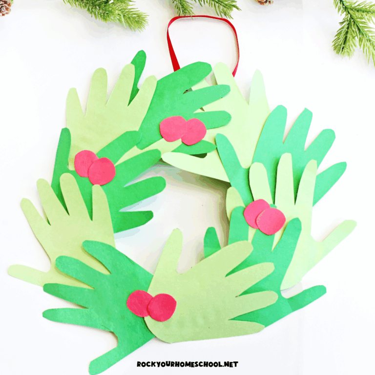 Example of paper Christmas handprint wreath craft for kids in green construction paper with red paper berries hanging on white door.