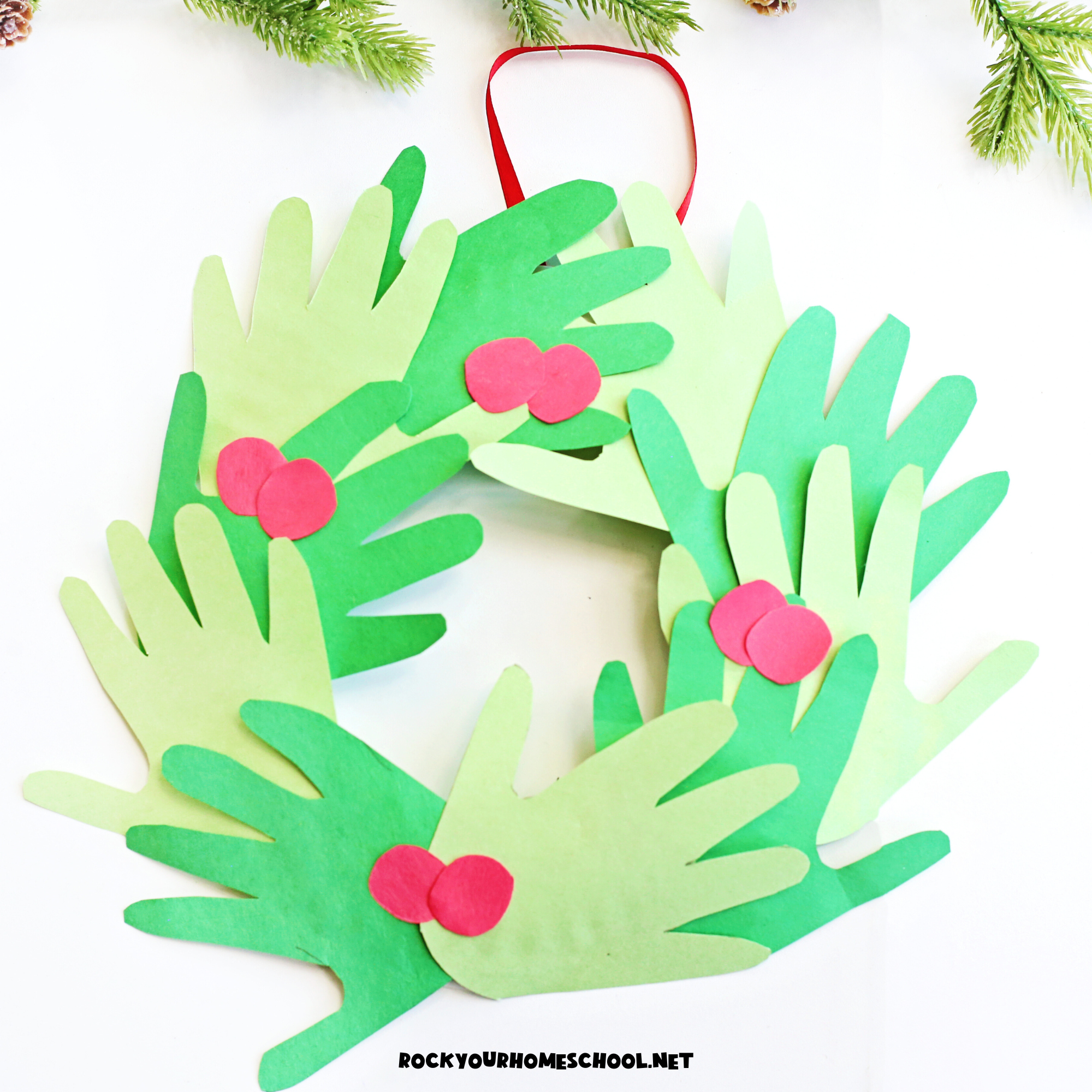 Example of paper Christmas handprint wreath craft for kids in green construction paper with red paper berries hanging on white door.