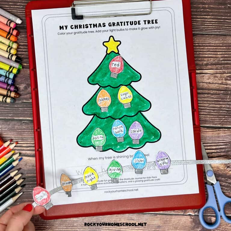Woman holding red clipboard with free printable Christmas gratitude tree activity and Christmas lights on silver ribbon.