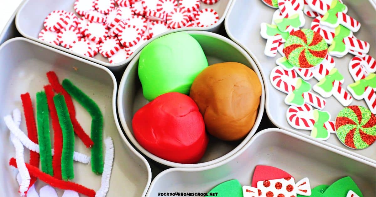 Gingerbread playdough activity tray with red, green, and brown playdough balls with pipe cleaners, holiday foam stickers, and peppermint embellishments.
