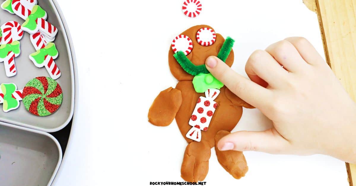 Child adding green pipe cleaner smile to gingerbread playdough character.
