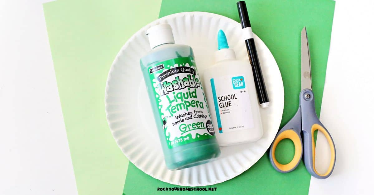 Light and dark green construction paper with green paint, glue, black marker, scissors, and paper plate.