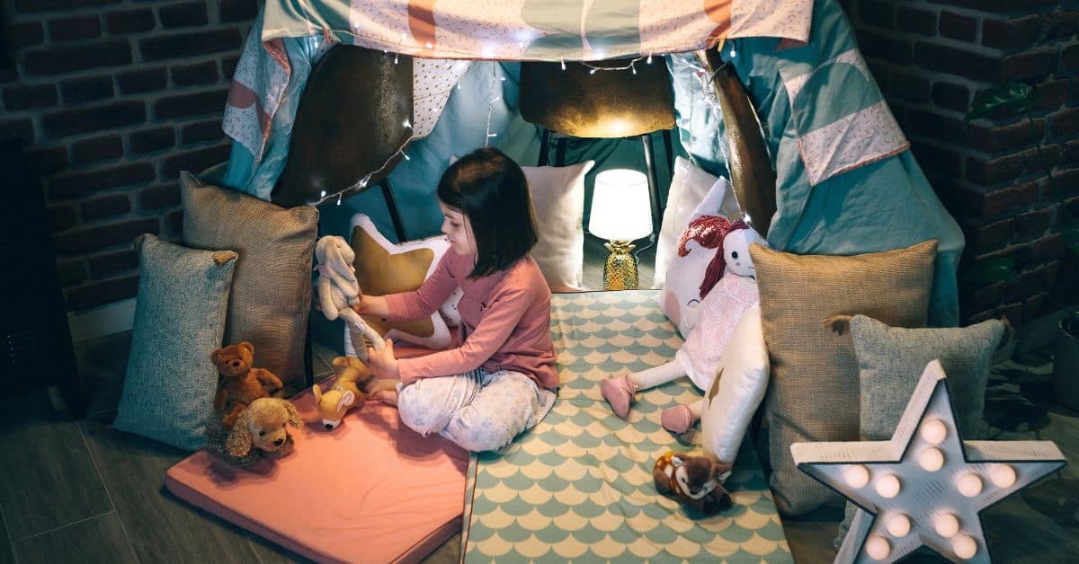Young girl using a child's play tent for a calm down corner while playing with stuffed animals.