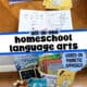 Two stacks of color-coded beginning readers from Learning Language Arts Through Literature displayed on a wood surface, with an open reader showing simple phonics text and illustrations plus display of resources available in this first grade homeschool language arts curriculum set.